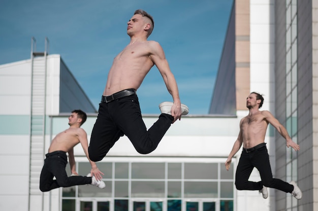 Vista lateral de tres bailarines de hip hop sin camisa posando en el aire
