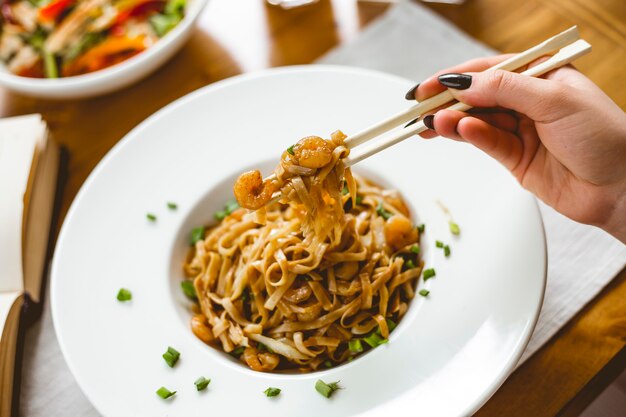 Vista lateral udon frito con camarones y cebolla tierna en un plato