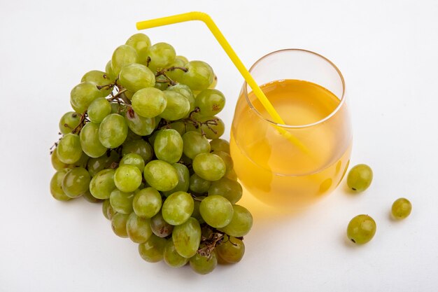 Vista lateral de uva blanca y jugo de uva con tubo para beber en vidrio sobre fondo blanco.