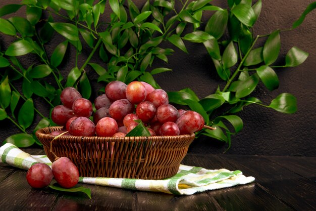 Vista lateral de uva dulce fresca en una cesta de mimbre sobre superficie de madera en la mesa de hojas verdes