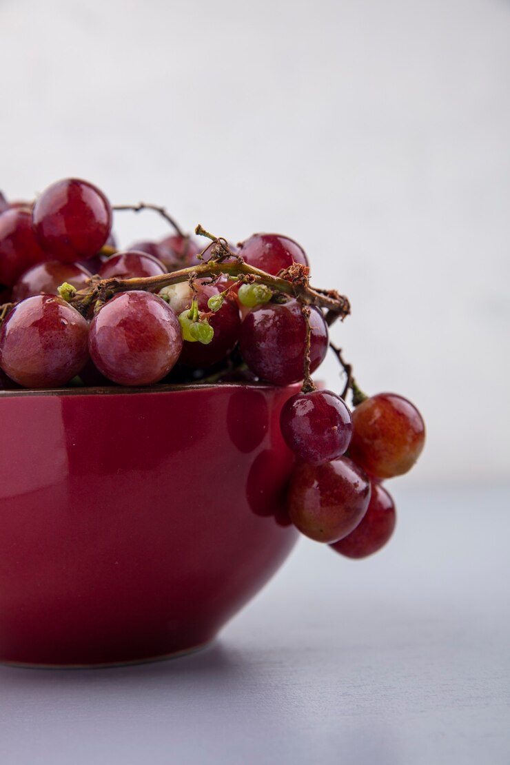 Foto gratuito vista lateral de uvas negras y rojas en un tazón sobre fondo gris