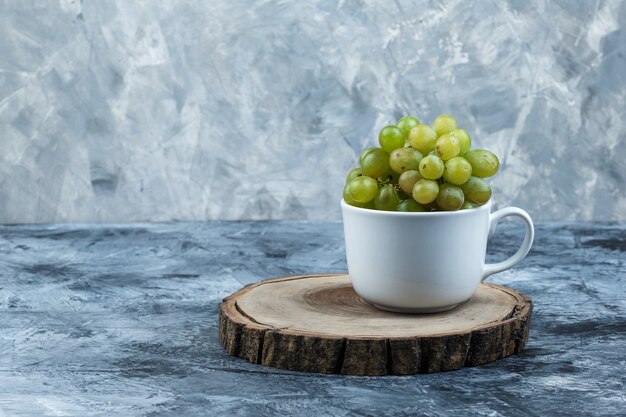 Vista lateral de uvas verdes en taza blanca sobre yeso sucio y fondo de madera. horizontal