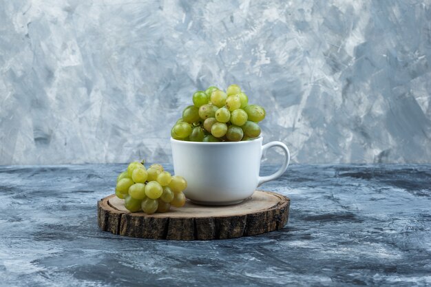 Vista lateral de uvas verdes en taza blanca sobre yeso sucio y fondo de madera. horizontal