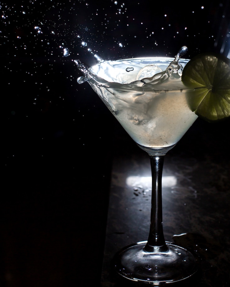 Foto gratuito vista lateral del vaso de martini y salpicaduras de hielo que cae sobre negro