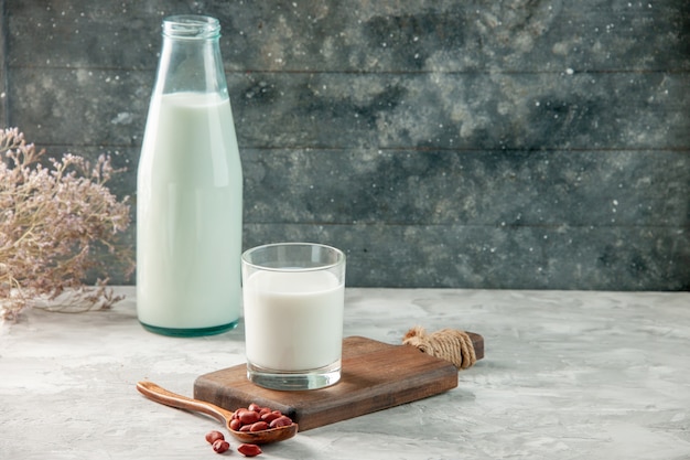 Vista lateral del vaso en la tabla de cortar de madera y una botella llena de leche y cacahuetes en la mesa gris