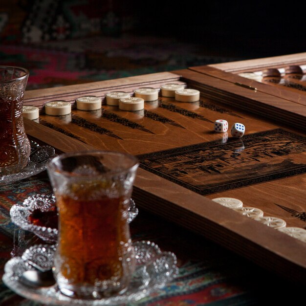 Vista lateral vaso de té con backgammon y mermelada en la mesa de alfombra