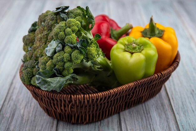 Vista lateral de verduras como brócoli y pimientos en canasta sobre fondo de madera