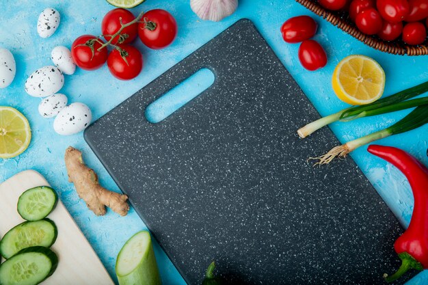 Vista lateral de verduras como jengibre huevo tomate y otros con limón y tabla para cortar sobre superficie azul