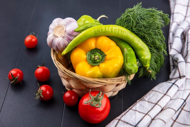 Vista lateral de verduras como pimienta ajo eneldo en canasta con tomates y tela escocesa en negro