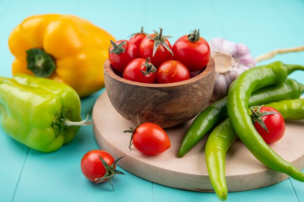 Vista lateral de verduras como tazón de fuente de tomate ajo pimiento sobre tabla de cortar en azul