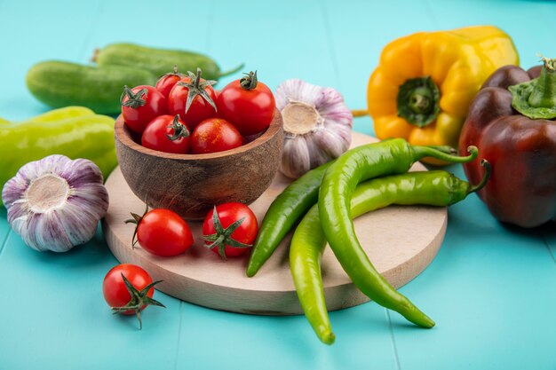 Vista lateral de las verduras como tazón de fuente de tomate ajo pimiento sobre tabla de cortar con pepinos en azul