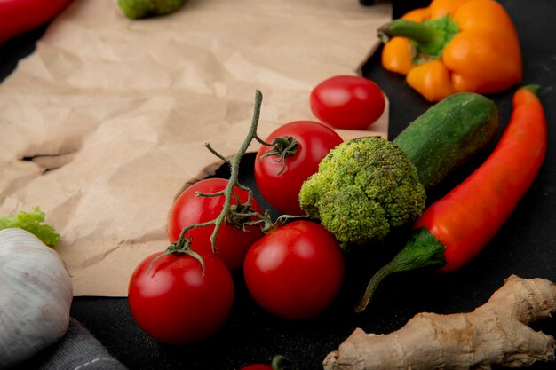 Vista lateral de verduras como tomate, brócoli y otros sobre fondo negro con copia espacio