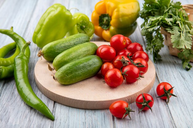 Vista lateral de verduras como tomate pepino en tabla de cortar con pimiento y cilantro en madera con espacio de copia