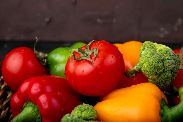 Vista lateral de verduras como tomates pimientos brócoli en superficie marrón