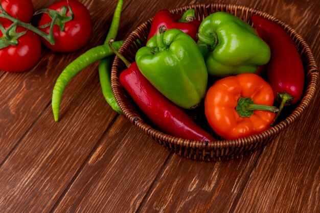 Vista lateral de verduras frescas coloridos pimientos chiles rojos en una cesta de mimbre en la mesa rústica de madera