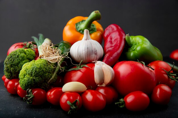 Vista lateral de verduras frescas maduras coloridos pimientos tomates ajo brócoli y cebolla verde sobre fondo negro