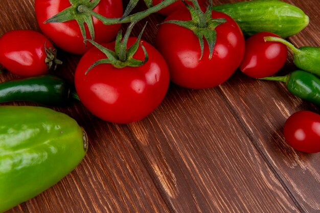 Vista lateral de verduras frescas, tomates maduros, pepinos, ají y coloridos pimientos en la mesa rústica de madera