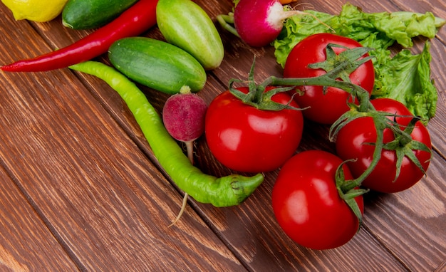 Vista lateral de verduras frescas tomates maduros pepinos pimientos verdes y rábano en madera rústica