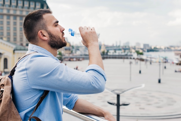 Foto gratuita vista lateral del viajero masculino beber agua de botella de plástico