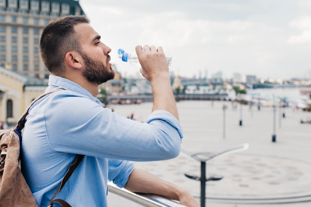 Vista lateral del viajero masculino beber agua de botella de plástico