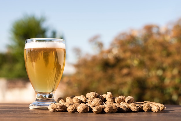 Vista lateral de vidrio con cerveza al lado de maní en la mesa