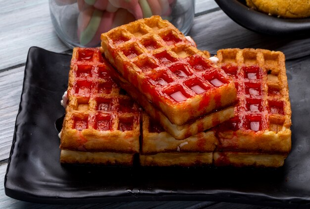 Vista lateral de waffles con jarabe de fresa en bandeja negra