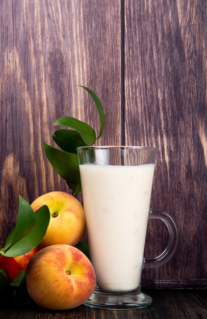 Vista lateral de yogurt en un vaso y duraznos maduros frescos en la mesa de madera rústica