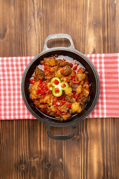 Vista lejana superior comida vegetal cocida que incluye verduras y carne dentro de un escritorio marrón de madera