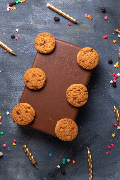 Vista lejana superior deliciosas galletas de chocolate en la caja marrón con té y velas en el fondo oscuro galleta galleta té dulce