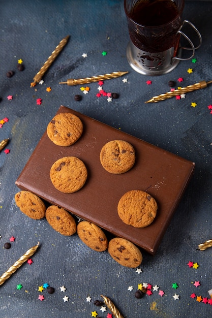 Vista lejana superior deliciosas galletas de chocolate en la caja marrón con velas de té en el fondo gris oscuro galleta galleta té dulce