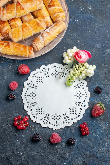 Foto gratuita vista lejana superior deliciosos brazaletes dulces con relleno dentro de la placa con bayas frescas en el escritorio oscuro, pastel de galletas dulces hornear pasteles