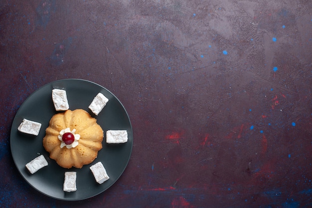 Vista lejana superior dulces de azúcar en polvo delicioso turrón con torta dentro de la placa sobre superficie oscura