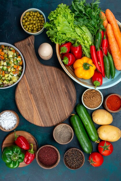 Vista lejana superior ensalada de verduras en rodajas salpicado con rodajas de pollo dentro de la placa con verduras frescas en el escritorio azul, almuerzo, ensalada, comida vegetal