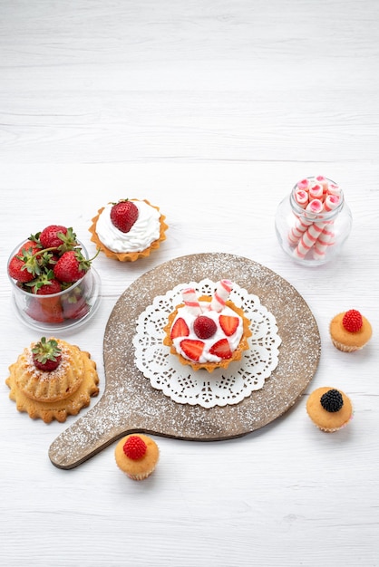 Vista lejana superior de la pequeña y deliciosa tarta con crema y tartas de fresas en rodajas en el escritorio blanco, tarta de baya dulce hornear frutas