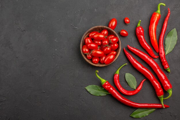 Vista lejana superior pimientos rojos y hojas de pago y un tazón de tomates cherry en la mesa negra