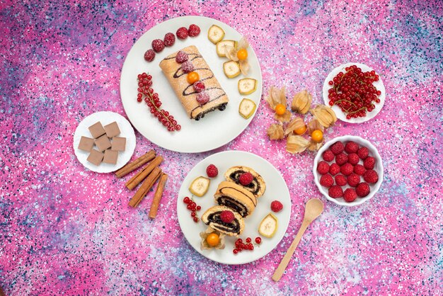 Vista lejana superior rollo de pastel con frutas dentro de la placa blanca sobre el fondo de color pastel galleta color dulce