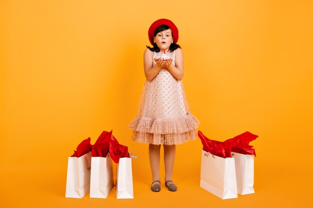 Vista de longitud completa de cumpleaños niña posando después de ir de compras. niño apaga velas en el pastel.