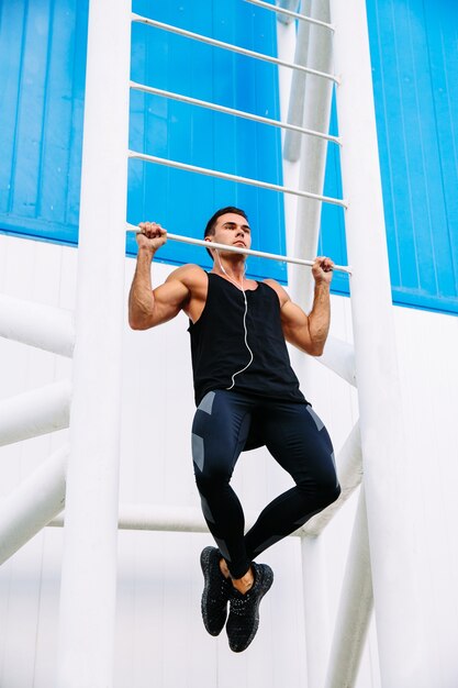 Vista de longitud completa de deportista fuerte motivado haciendo pull ups escuchando música