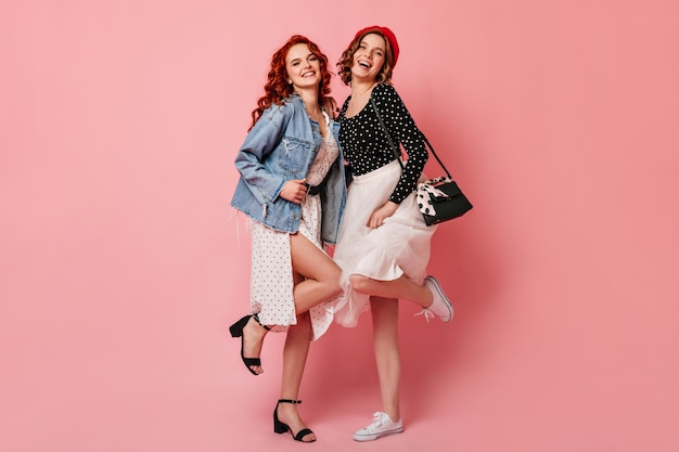 Vista de longitud completa de elegantes chicas bailando con una sonrisa. Foto de estudio de amigos en ropa casual.