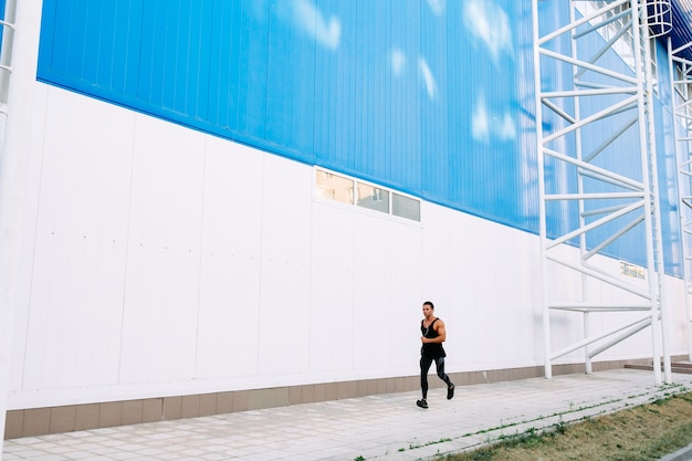 Vista de longitud completa del joven deportista en ropa deportiva negra durante correr al aire libre.