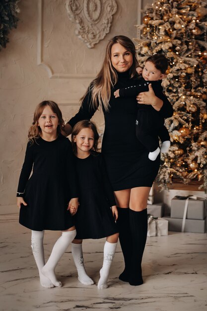 Vista de longitud completa de la madre feliz con sus hijos pequeños juntos cerca del árbol de Navidad en casa. Concepto de felices vacaciones