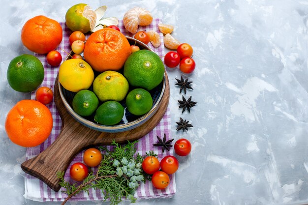 Vista media superior agria mandarinas frescas con limones y ciruelas en el escritorio blanco cítricos frutas tropicales exóticas vitamina agria