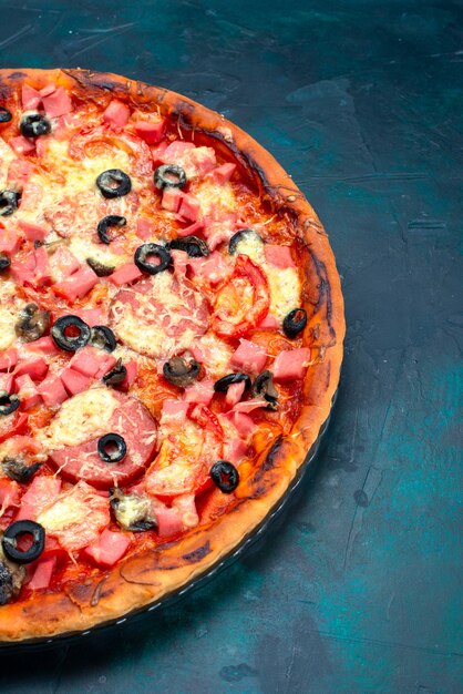 Vista media superior horneada deliciosa pizza con aceitunas, salchichas y queso en el escritorio azul.