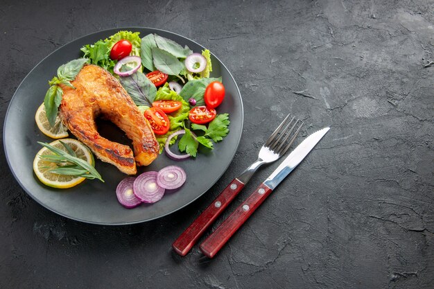 Vista media superior sabroso pescado cocido con verduras frescas y cubiertos sobre un fondo oscuro plato de fotos de alimentos color crudo carne mariscos