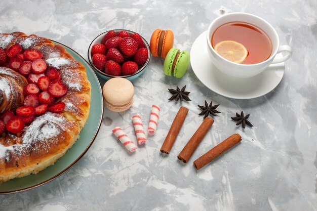 Vista media taza de té con macarons franceses y pastel sobre una superficie blanca clara