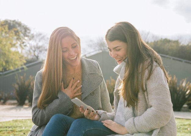 Vista media de la vista lateral de dos mujeres jóvenes que miran el teléfono en el parque