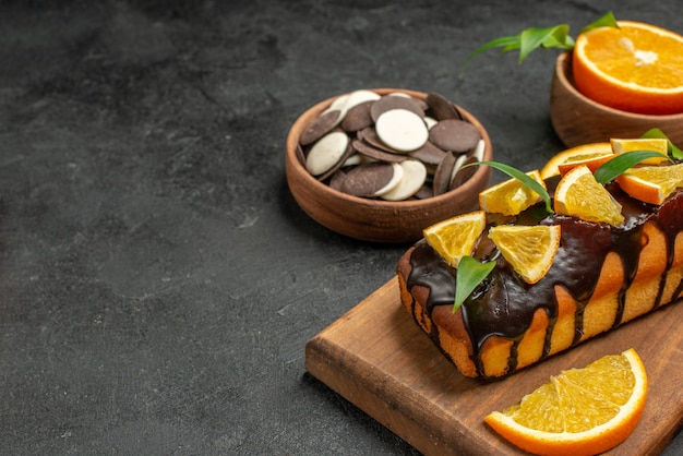 Foto gratuita vista de medio tiro de sabrosos pasteles cortan naranjas con galletas en la tabla de cortar en la mesa oscura