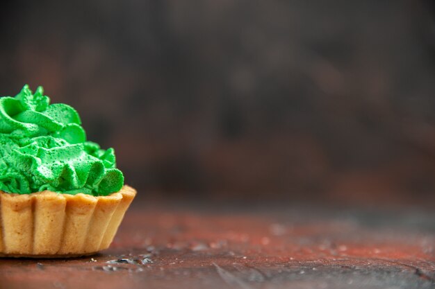 Vista de la mitad frontal tarta pequeña con crema pastelera verde sobre una mesa de color rojo oscuro con espacio de copia