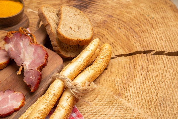 Vista de la mitad inferior becon rebanadas sobre una tabla de cortar pan blanco y marrón cúrcuma en un tazón pequeño sobre la mesa de madera