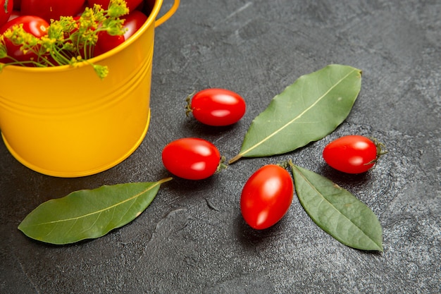 Foto gratuita vista de la mitad inferior cubo amarillo de tomates cherry y flores de eneldo y hojas de laurel sobre el fondo oscuro